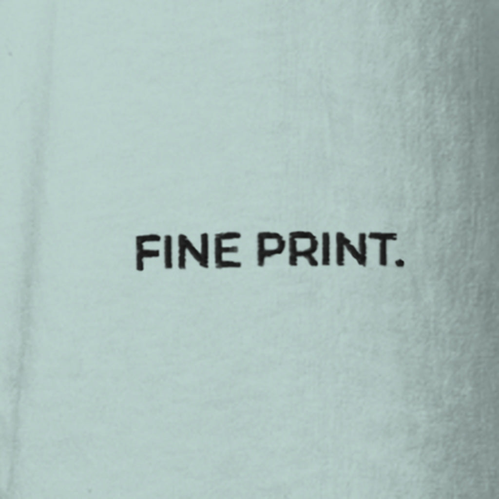 Close-up of the left sleeve of the Fine Print Tee: FINE PRINT. embroidered in small black capitals on Agave cotton.