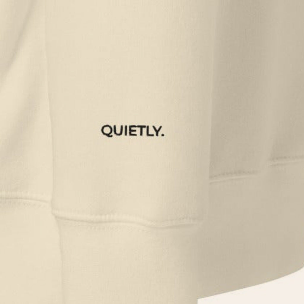 Close-up of the left cuff of the Morning Edition Crew, embroidered QUIETLY. in black thread.