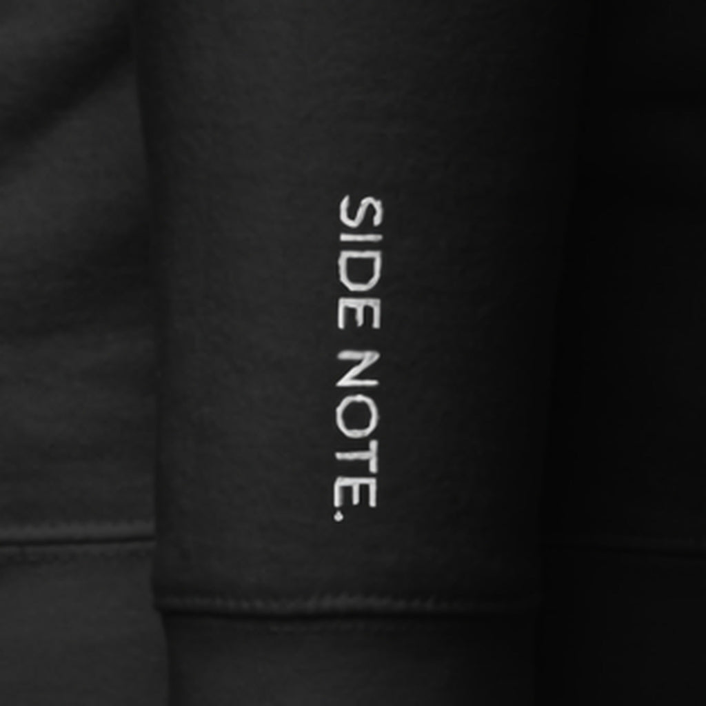 Close-up of the left cuff of the Side Note Hoodie: SIDE NOTE. embroidered vertically in white thread on black fleece.