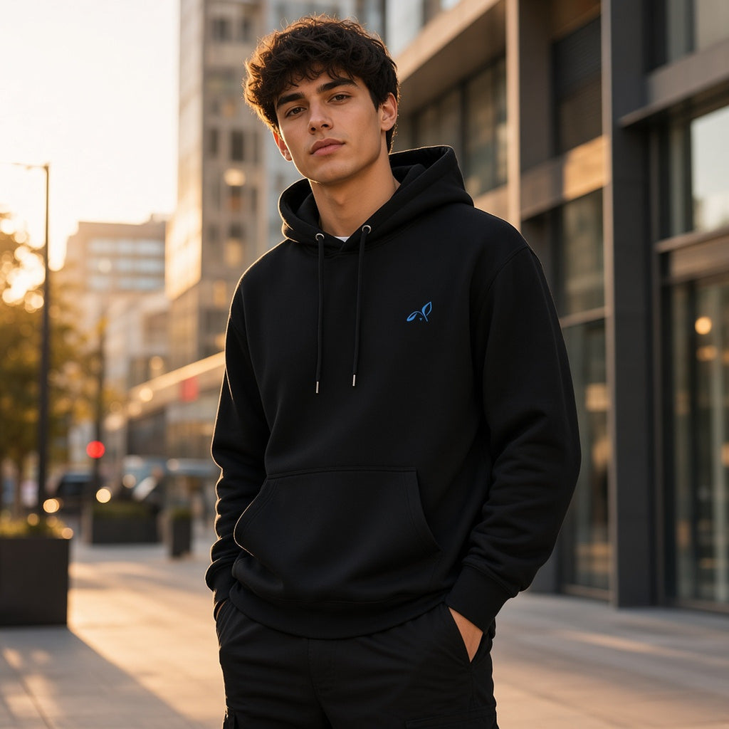 Model wearing the black LOUPI GANG Side Note Hoodie on a city street at golden hour, light blue embroidered rabbit on the left chest.